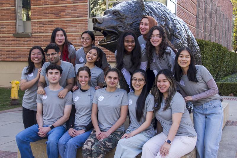 group of 14 students posed in front of the bruin bear statue