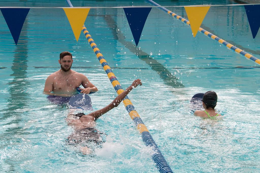An instructor watching two students swim in the lap lanes of a pool