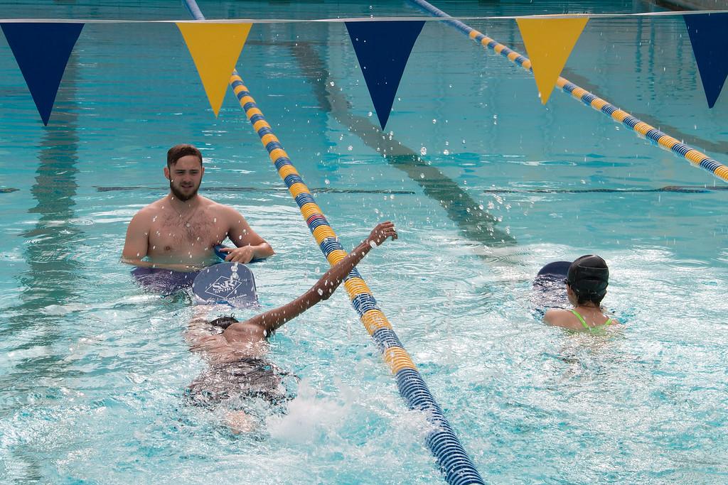 An instructor watching two students swim in the lap lanes of a pool