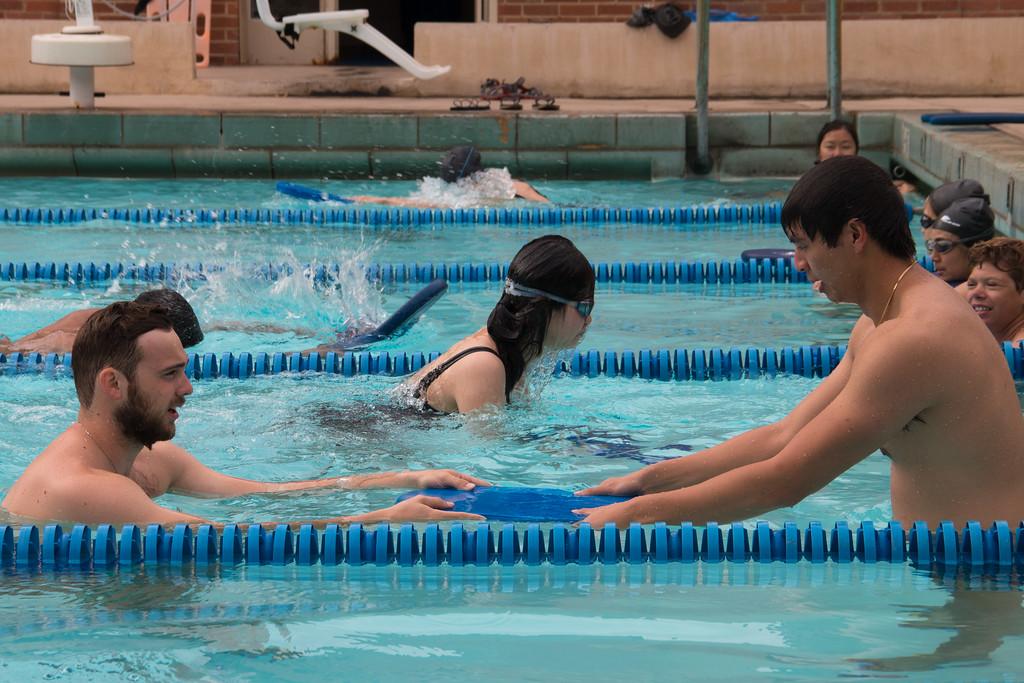 Instructor in the lap lanes of the pool with a student and a kick board 