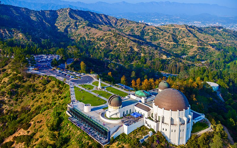 A bird's eye view of the Griffith Observatory and mountains surrounding it. 