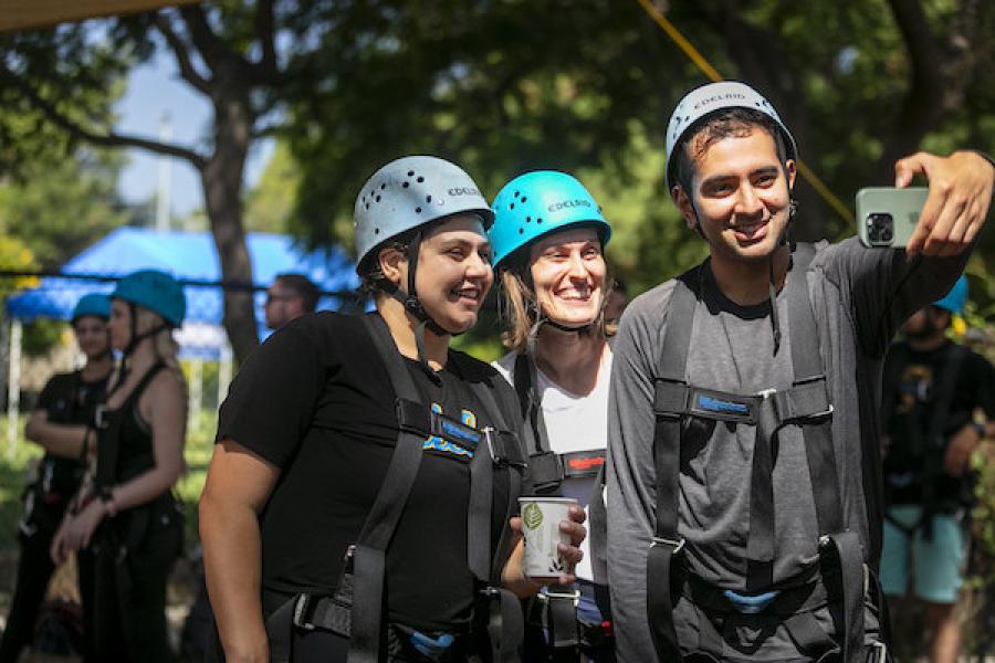 group of three participants taking a selfie wearing helmets and high ropes harnesses