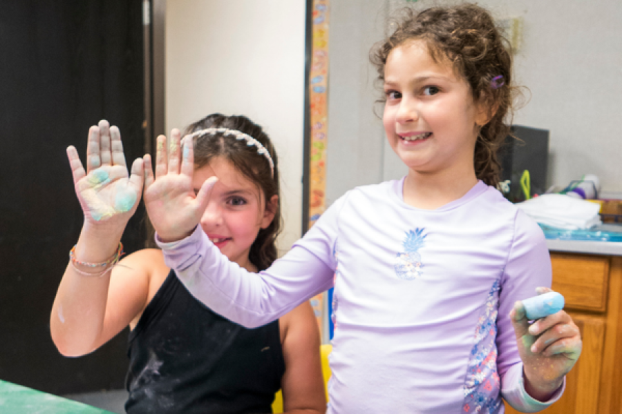 two girls smiling and showing the paint on their hands from a craft