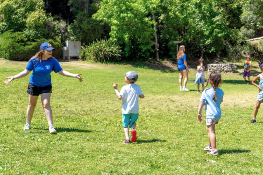 photo of a group of kids playing outside in the grass with a camp counselor