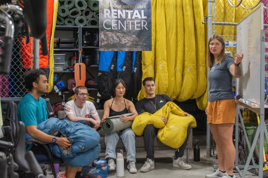 People holding sleeping bags and sleep mat watching instructor